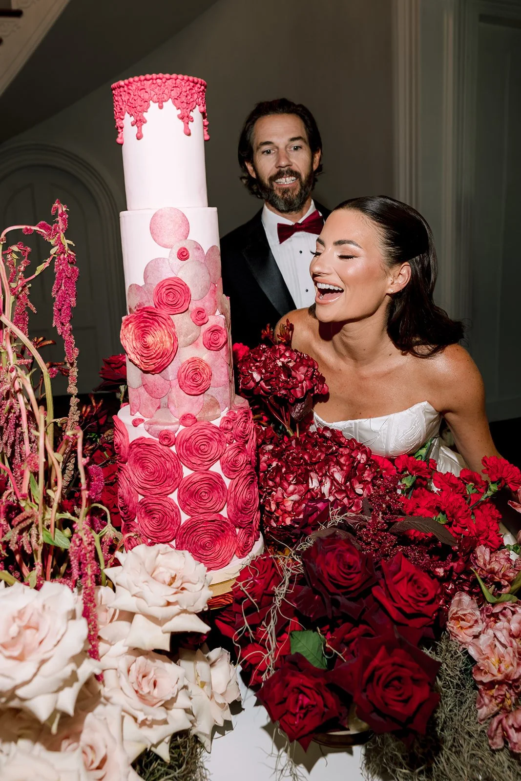 Bride and groom beside a bold red and blush floral wedding cake