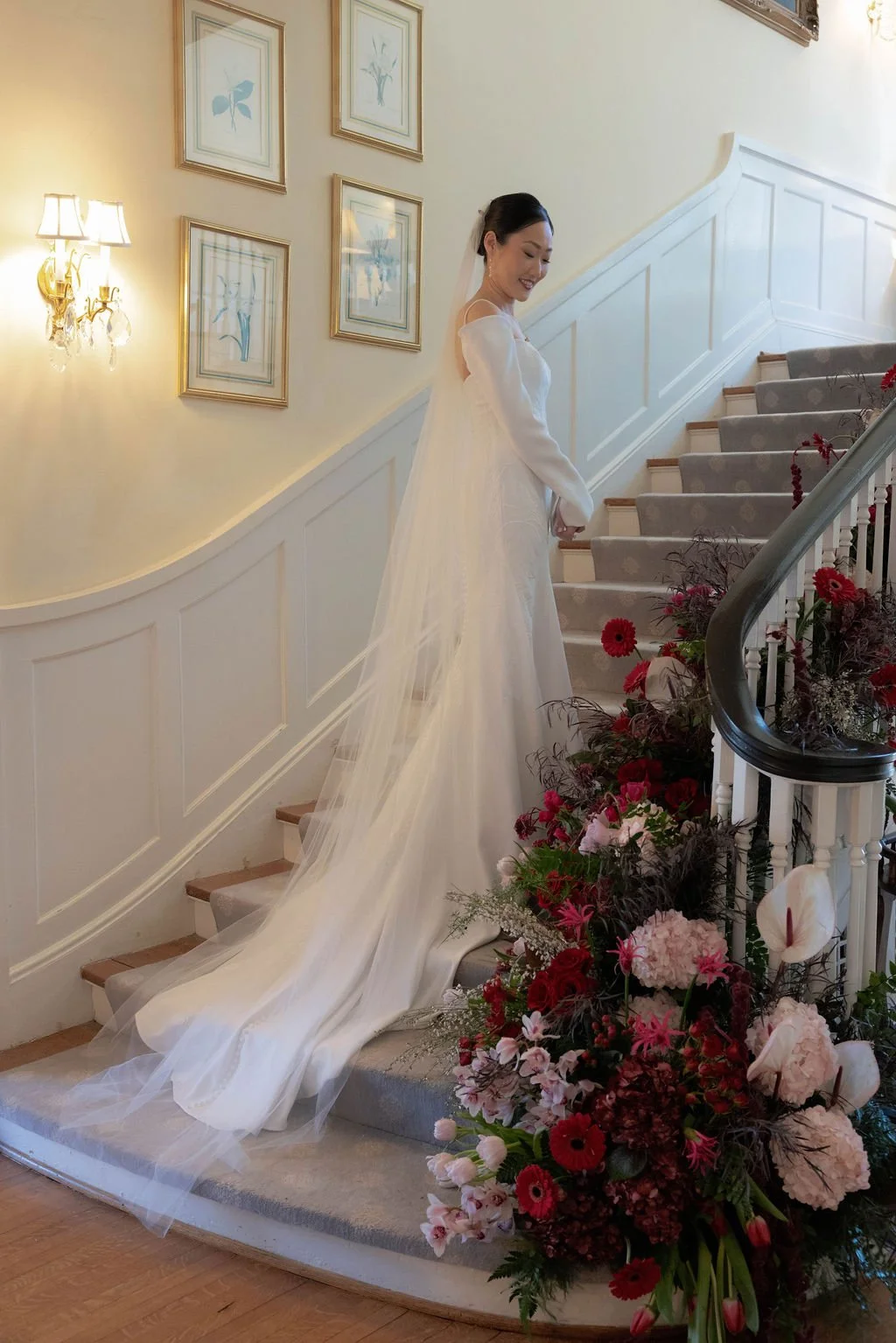 Bride on a grand staircase with a lush red and blush stair arrangement