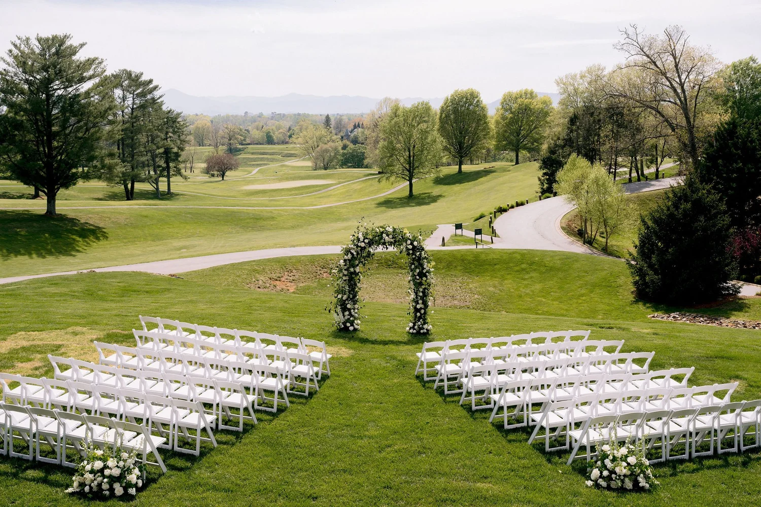 Garden ceremony arch on a green lawn with rows of white chairs