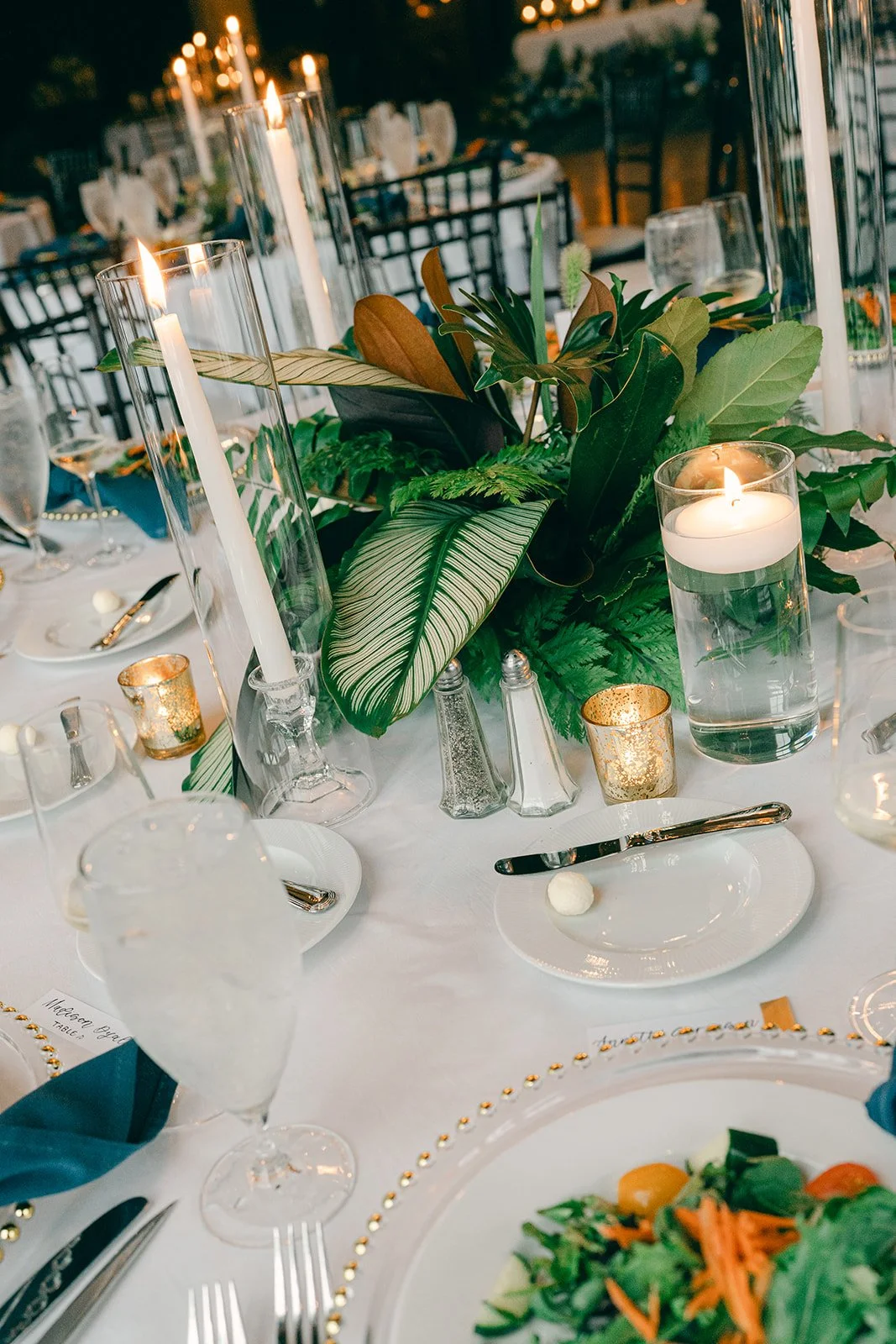 Reception tablescape with tropical foliage, taper candles and gold accents