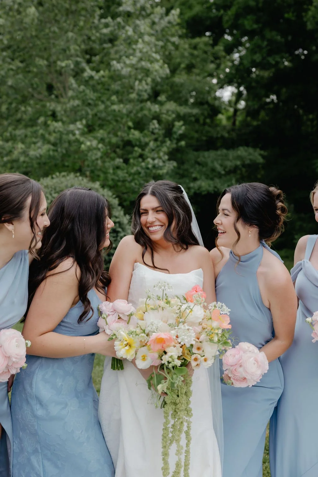 Bride and bridesmaids in dusty blue holding pastel garden bouquets