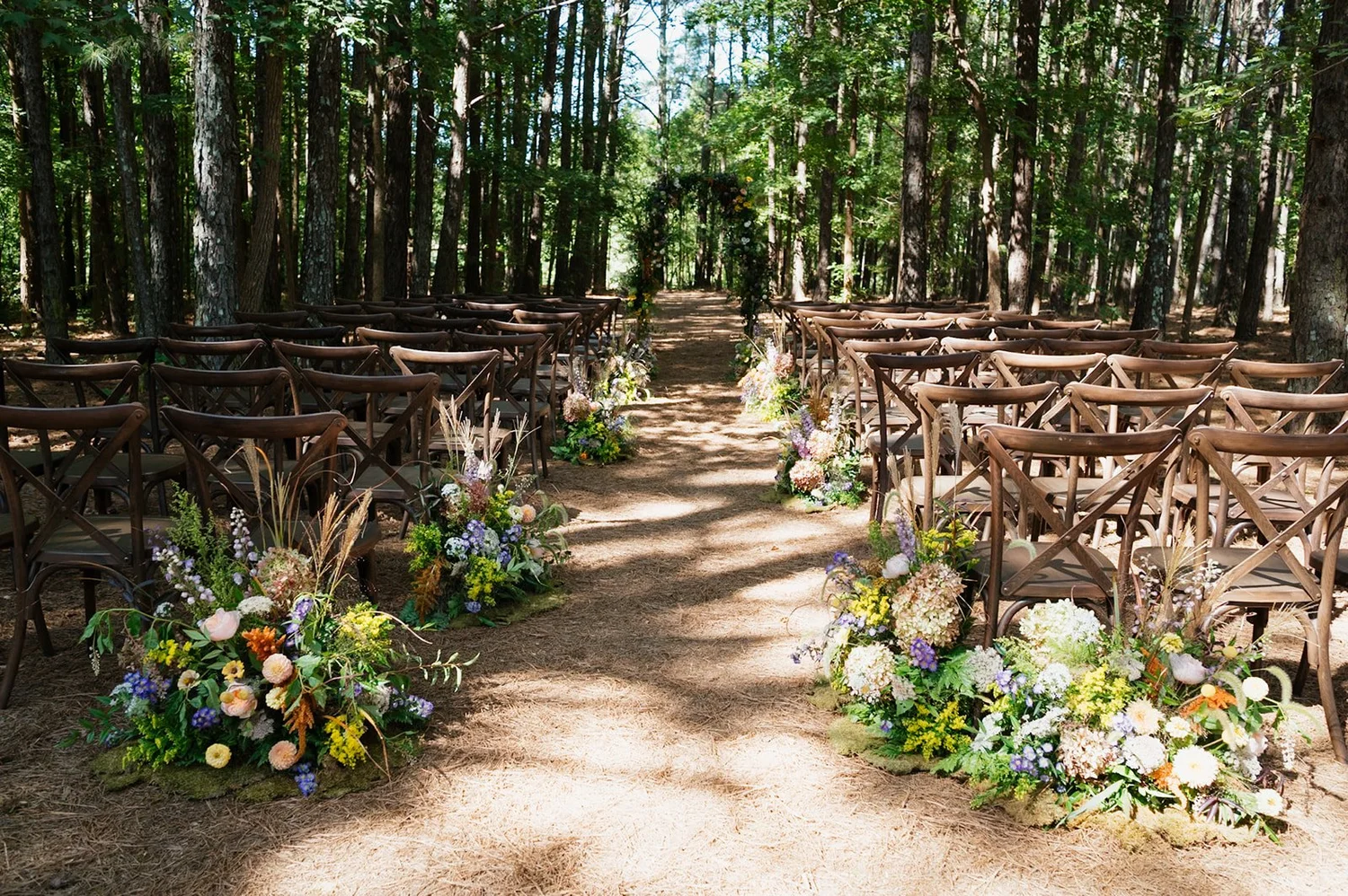 Woodland ceremony aisle lined with wildflower meadow arrangements