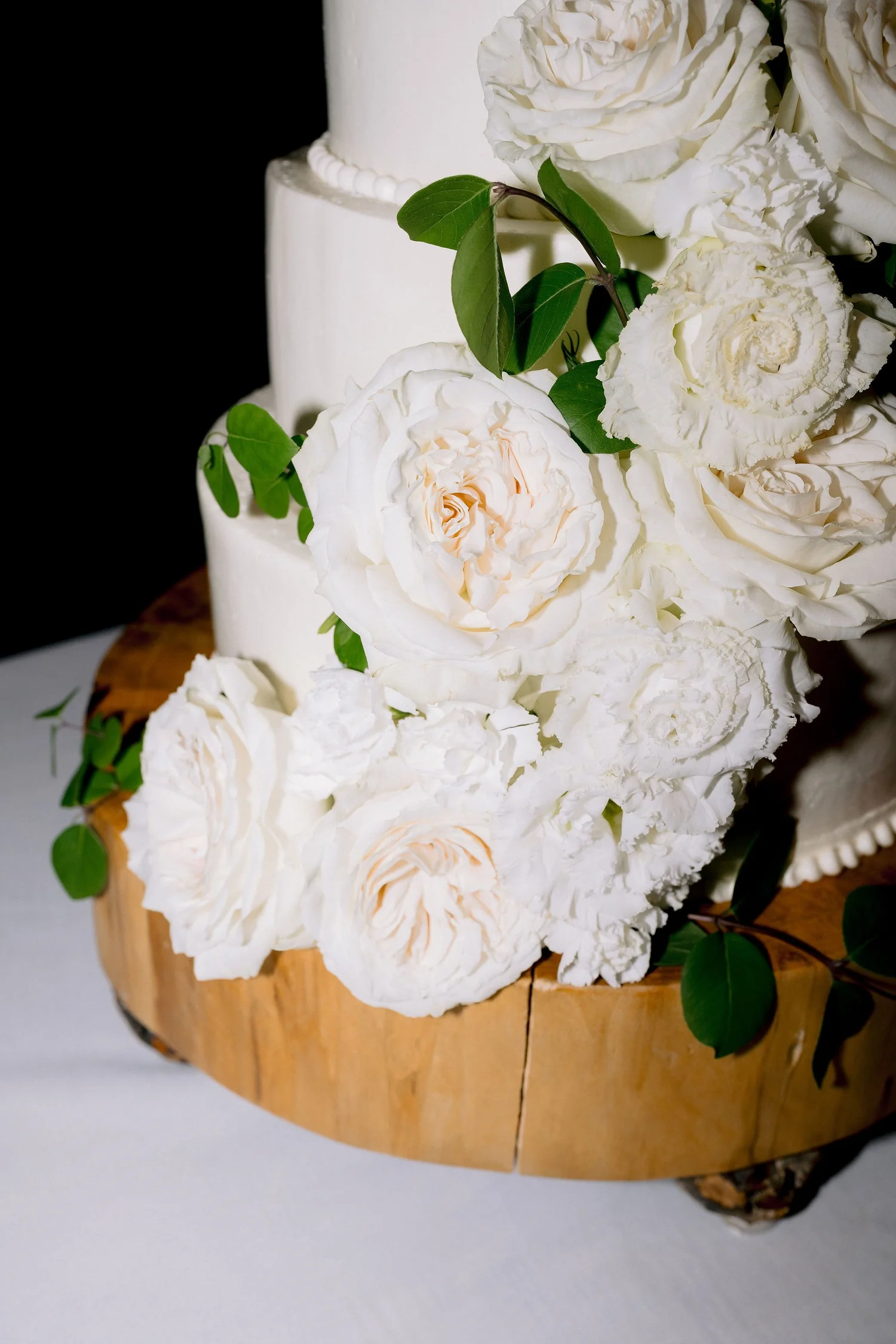 Three-tier white wedding cake trimmed with garden roses on a wood stand